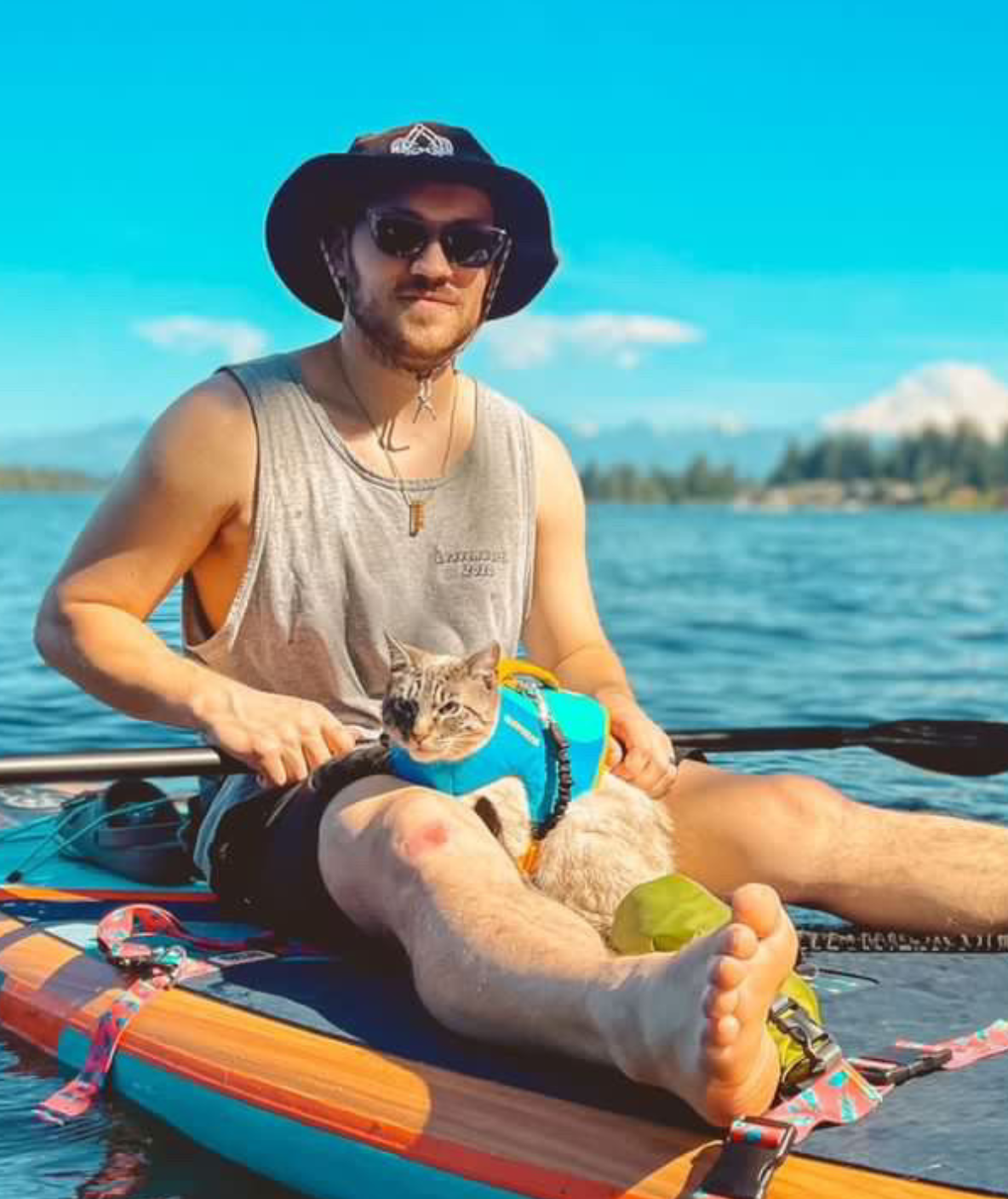 person with cat in a life jacket sitting on a paddle board